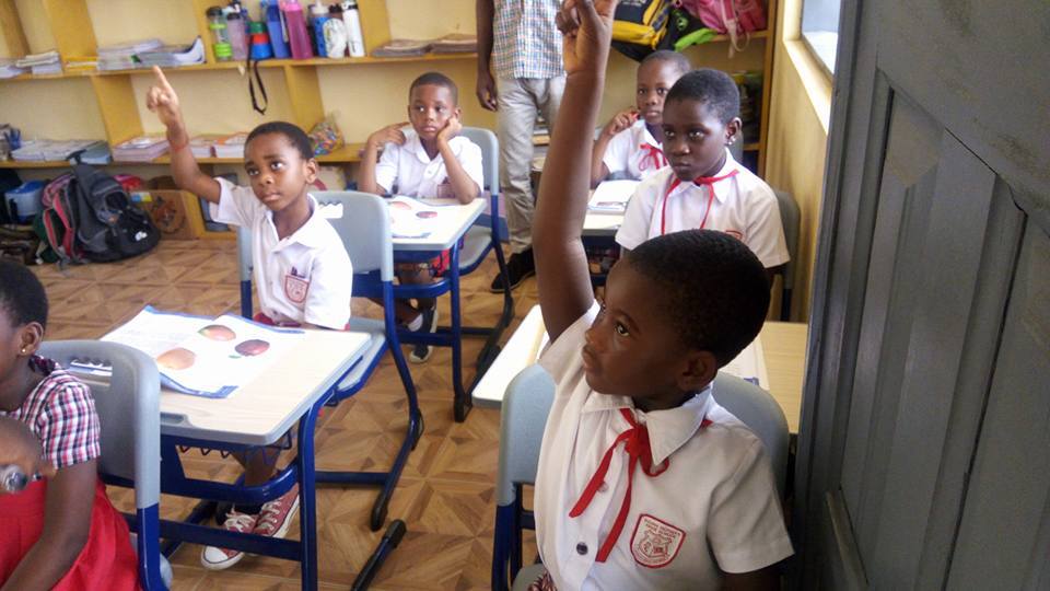 Students enthusiastically raising hands in a classroom supported by PROaid Africa